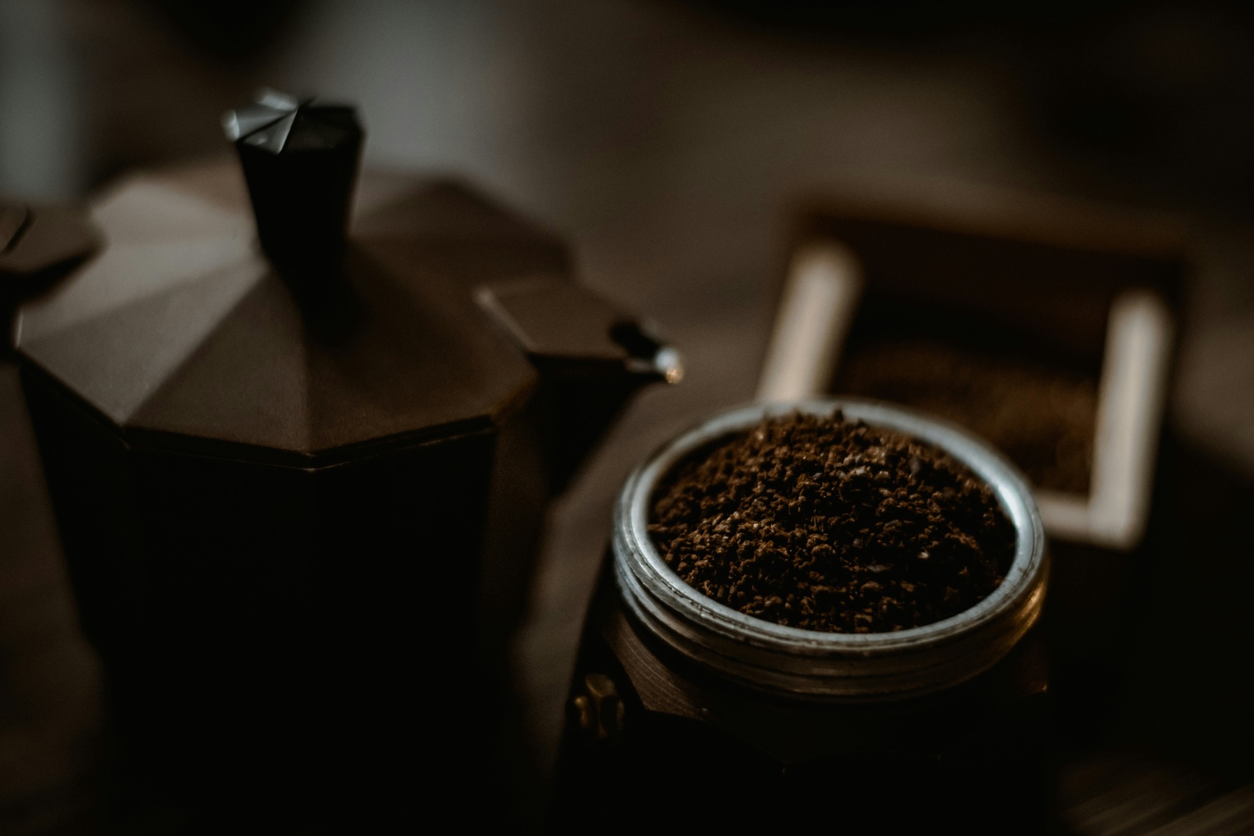 An open moka pot beside its basket of ground coffee
