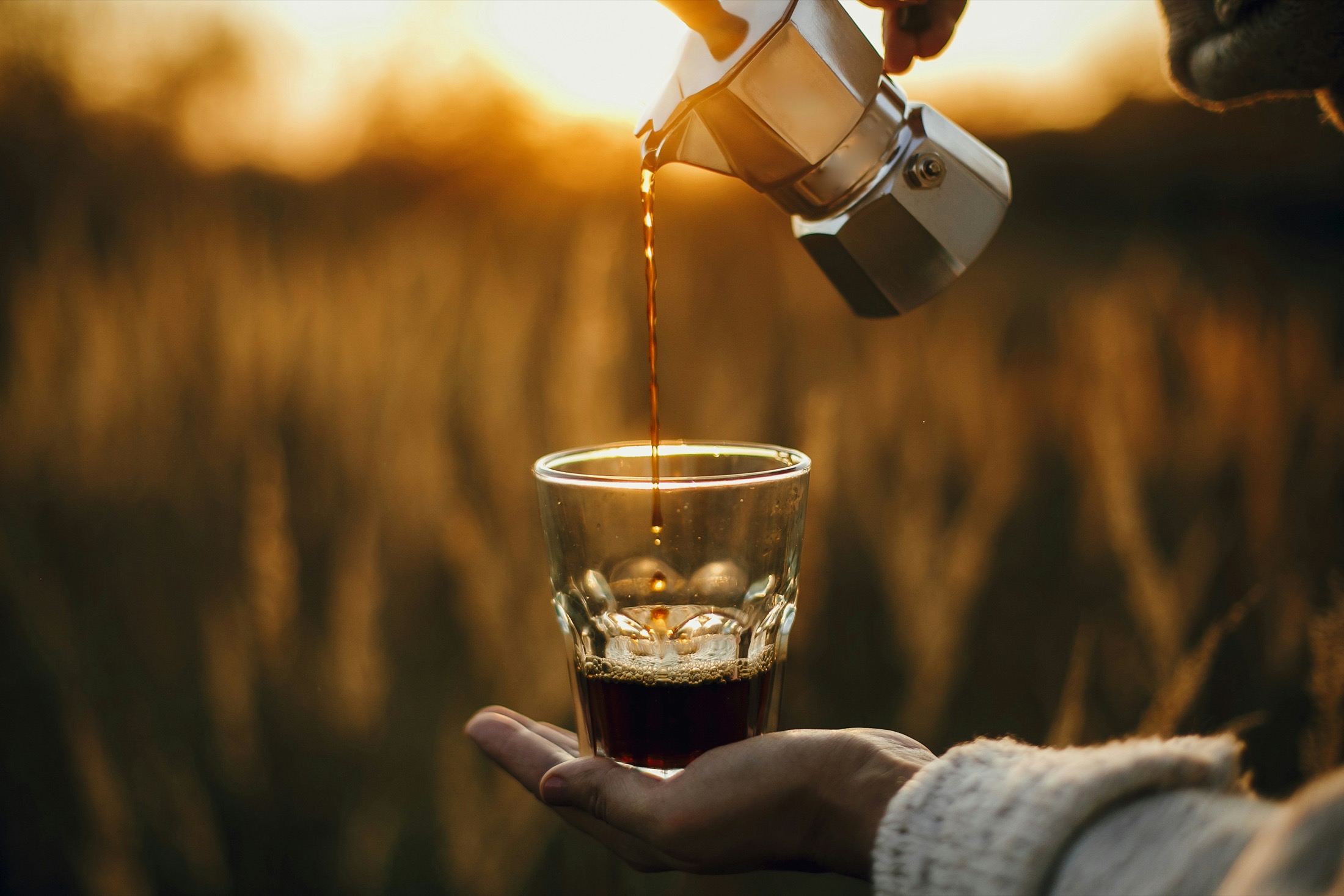 Coffee pouring from a silver moka pot into a glass in golden afternoon light